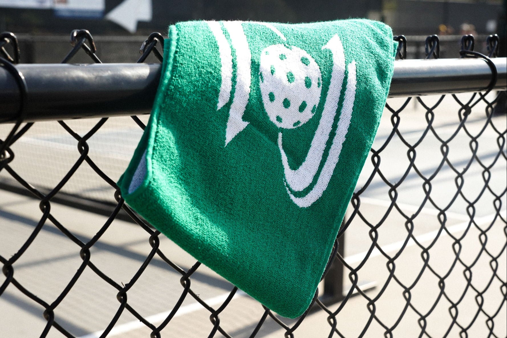 Green Dillz pickleball towel hanging on a court fence